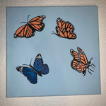 This image is of an art piece of four butterflies. Three are orange and one is blue. 