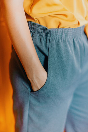 A photographic image cropped to display a person's arm tucked into the pocket of their blue, elastic waistbanded pants. 