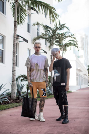 A photographic image of two boys standing on a pink sidewalk in front of a white apartment complex and palm trees.