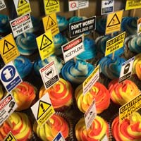 Over a dozen cupcakes with half looking like red/yellow swirling frosting and the other with blue/white swirling frosting. Each one has a safety sign. Click here for a larger picture.