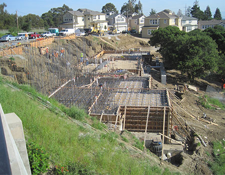 An image of an out of level project. There is a significant amount of form boards for a stem wall and rebar to support the out of level foundation. The concrete has not been fully poured.