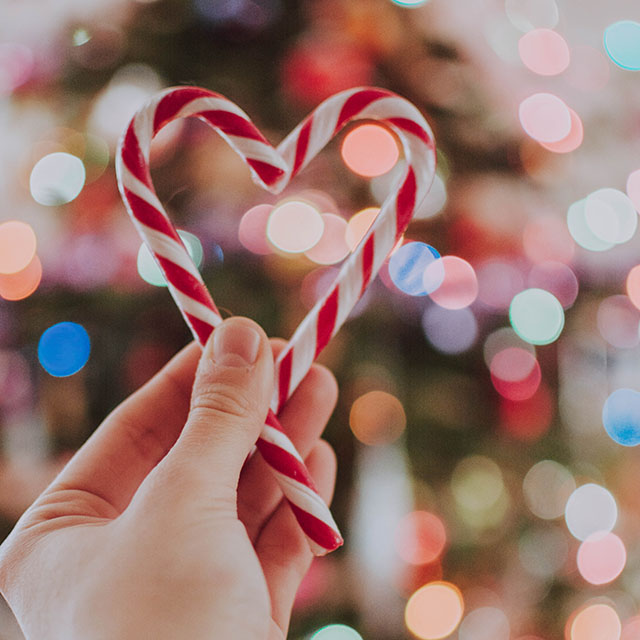A hand holds two candy canes to shape a heart.
