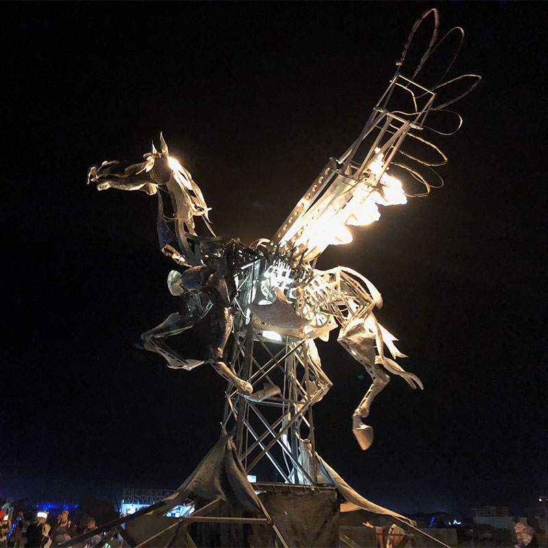 A mechanical horse with wings lit up with flames in the dark of the night