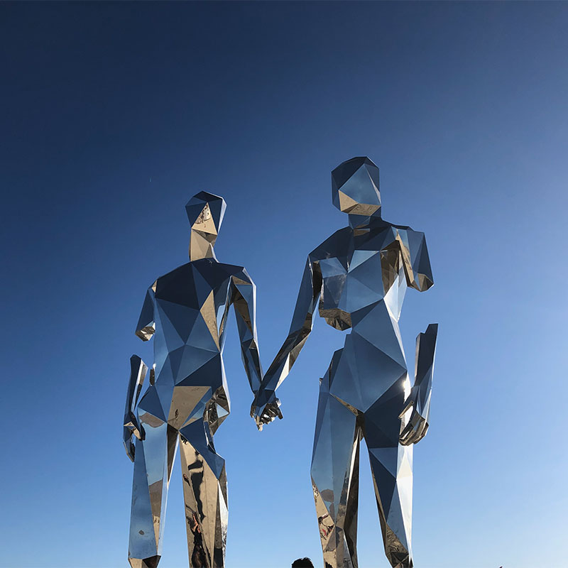 A metallic sculpture of a couple holding hands with a blue gradient sky in the background