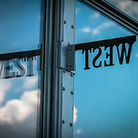 A metal West sign reflected in a window pane.