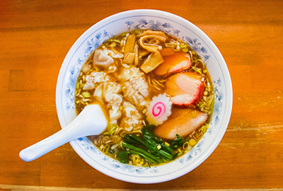 Traditional Japanese ramen with narutomaki, dumplings, sliced pork and bamboo shoots in a blue-patterned bowl