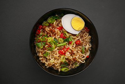 Bowl of spicy instant noodles topped with green onions, red chili peppers and half a boiled egg