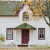 Quaint white home with olive-green roofing and a red door.