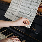 Hands flip through a music book while sitting at a piano.