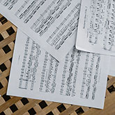 Three pieces of sheet music sprawled on a table made with thin cross-crossing pieces of wood.