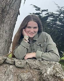 Picture of me wearing a green coat and resting my elbows on an old stone wall.