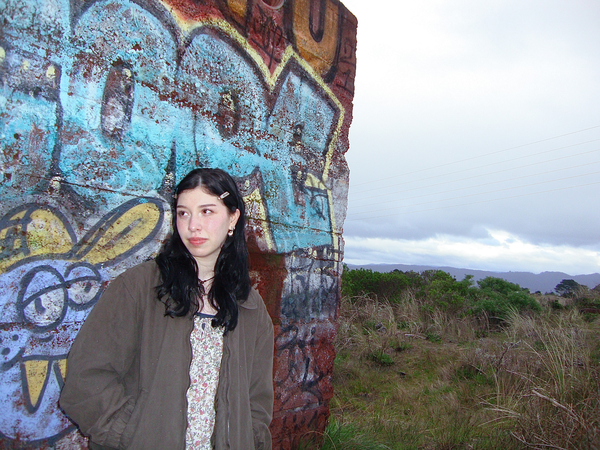 Picture of woman standing against a graffitied brick wall.