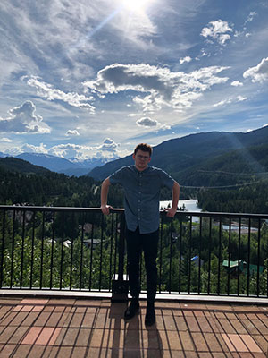 I am standing with a background of trees, mountains, and the sky from a terrace.